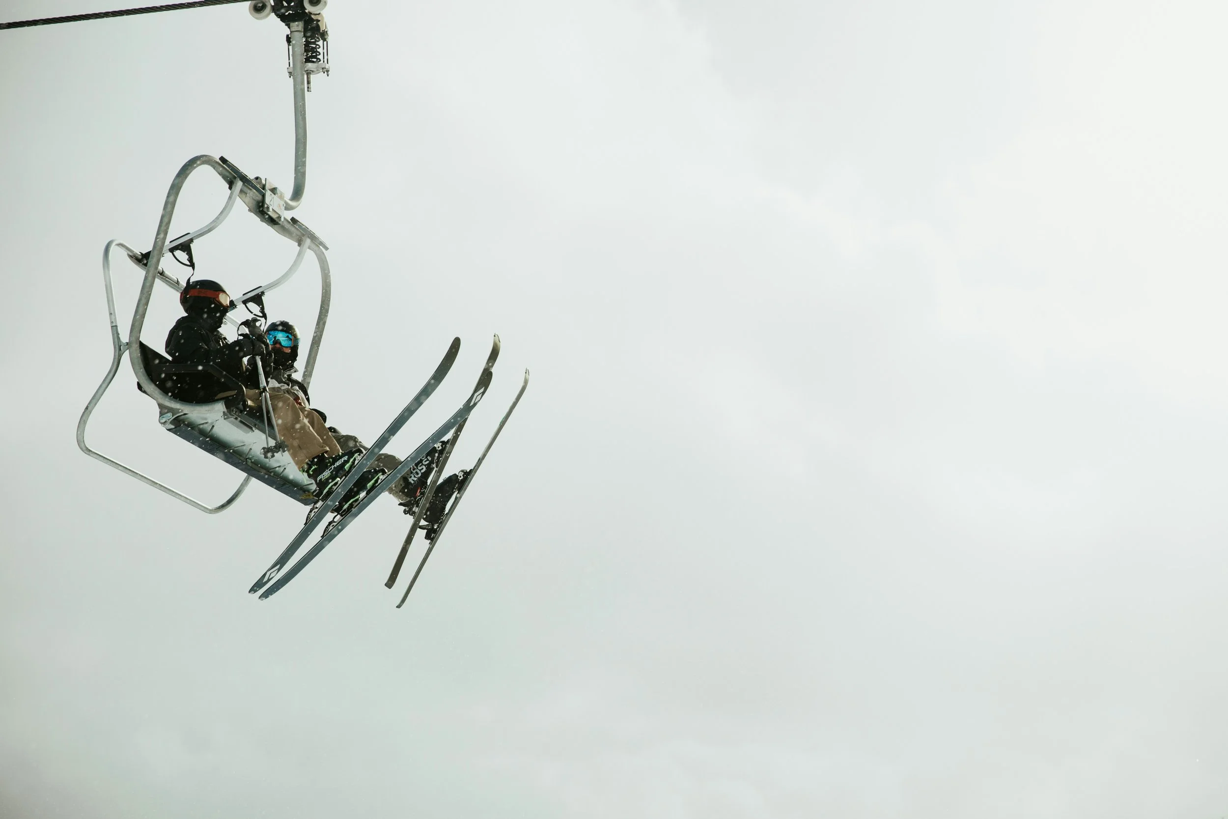 Two skiers point their skis upward as they rest on a chairlift.