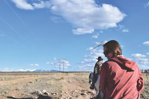 A girl in a red coat smiles as she lacks back at the camera on a Colorado  Trail Ride.
