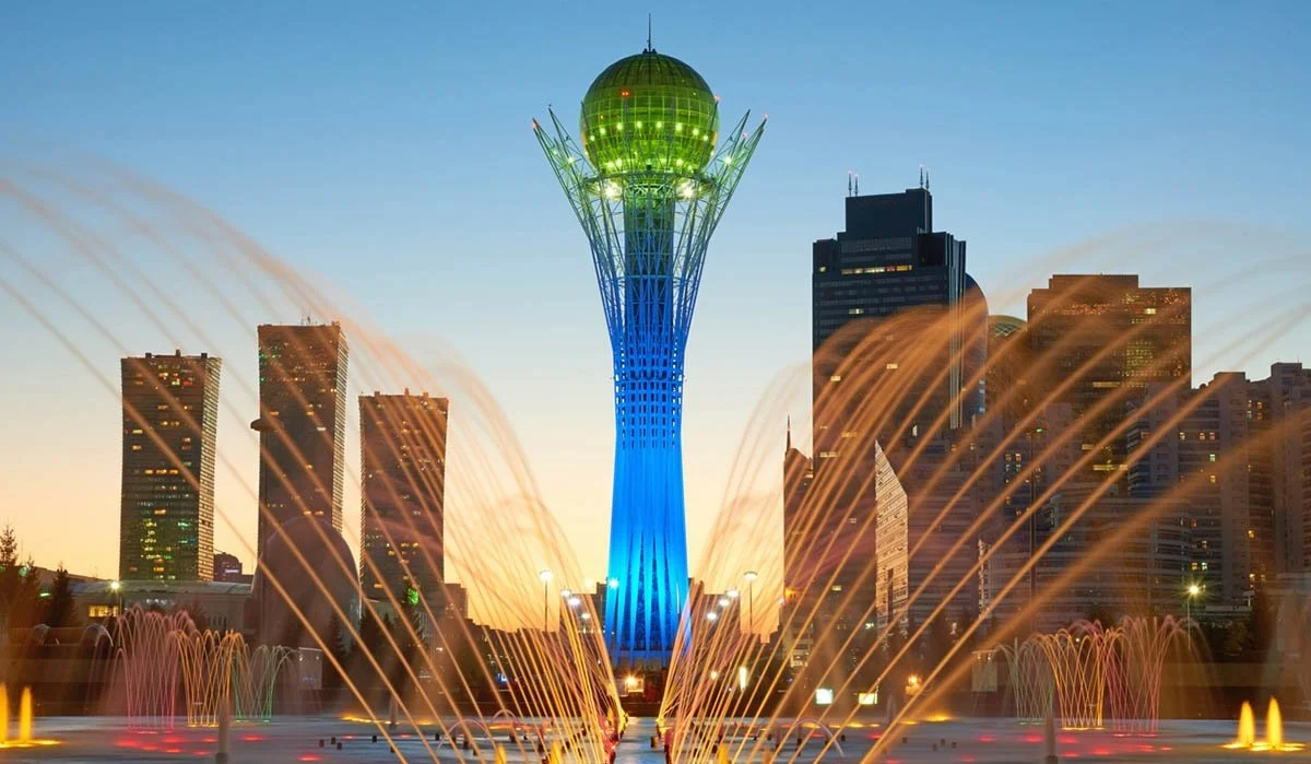 Baiterek tower covered in green and blue stands tall along skyscrapers and fountains.