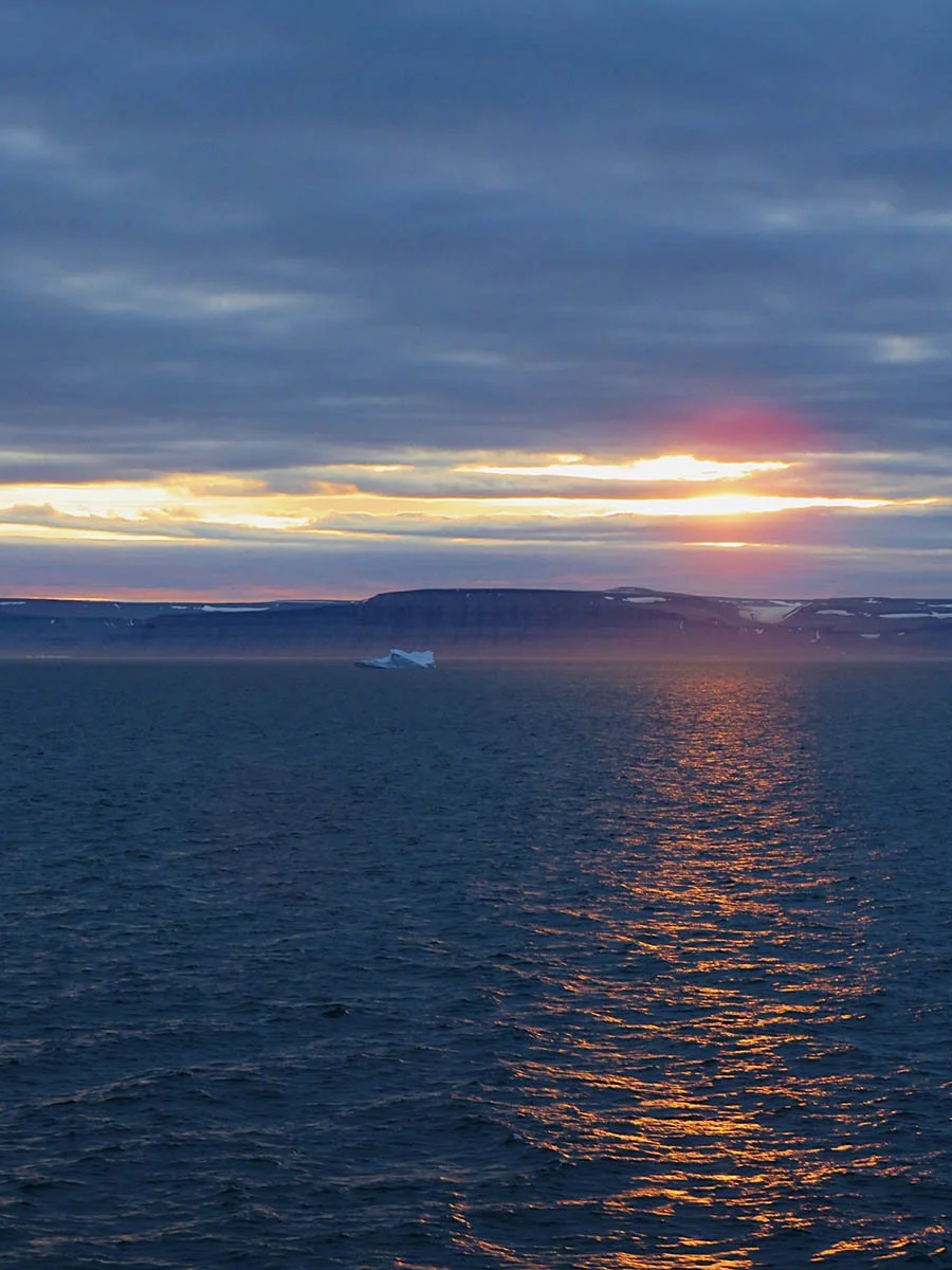 A sunset reflects over the water above fjords in Greenland.