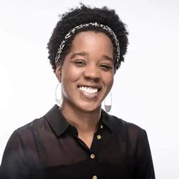 Portrait of a smiling woman with curly hair wearing a black shirt and a headband, against a white background.