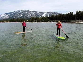 A couple in red jackets stand up paddleboards along Lake Tahoe.