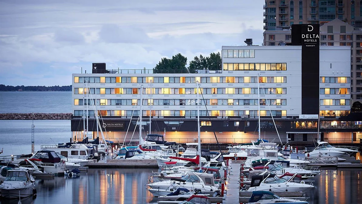 Lights from the Delta hotel reflect in the water surrounded by a dock of boats in Kingston.