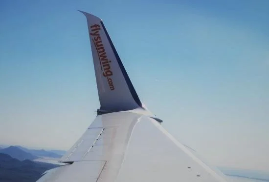 Sunwing airlines cruises over sea and mountains.