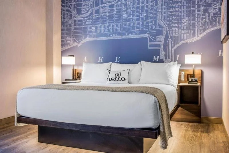 A white bed sits in front of a large, blue map photo at the Cambria.