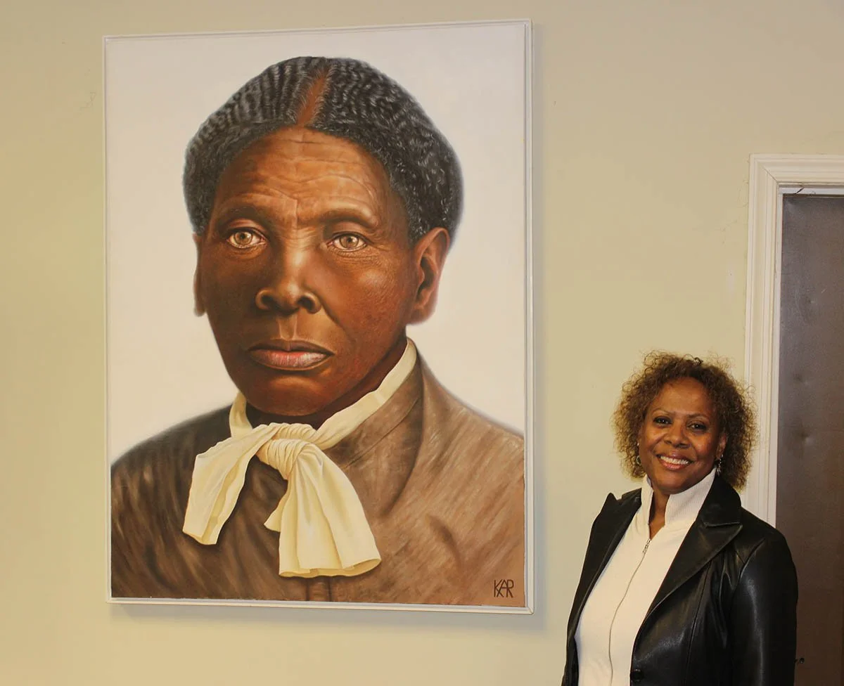 Community activist, singer and historian, Linda Harris  standing in front of a portrait of Harriet Tubman.