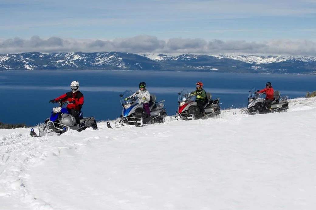 A group of 4 snow-mobile in front of the mountains surrounding Lake Tahoe.