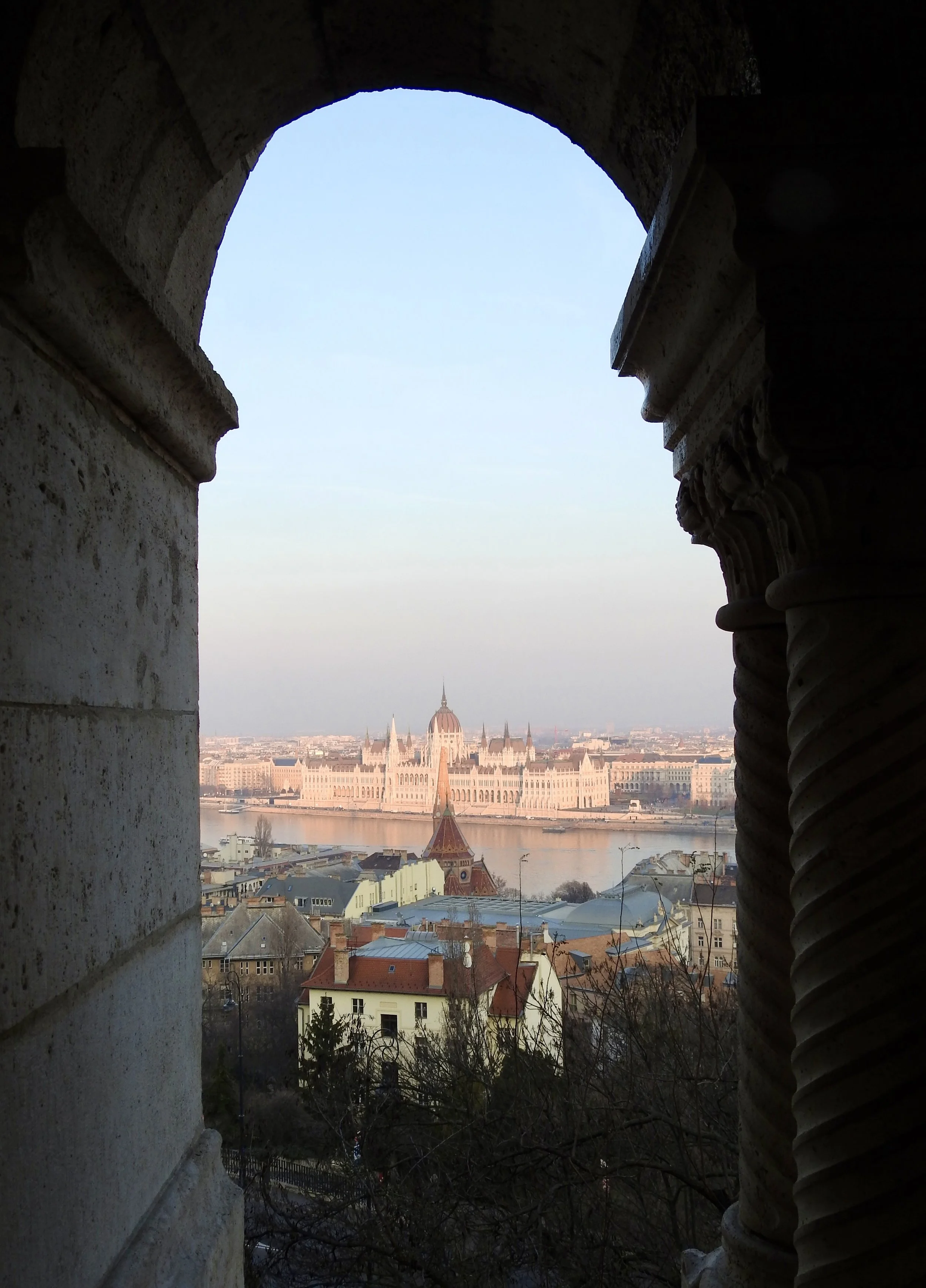 View of the Hungarian Parliament Building seen through a stone window frame from a high vantage point in Budapest.