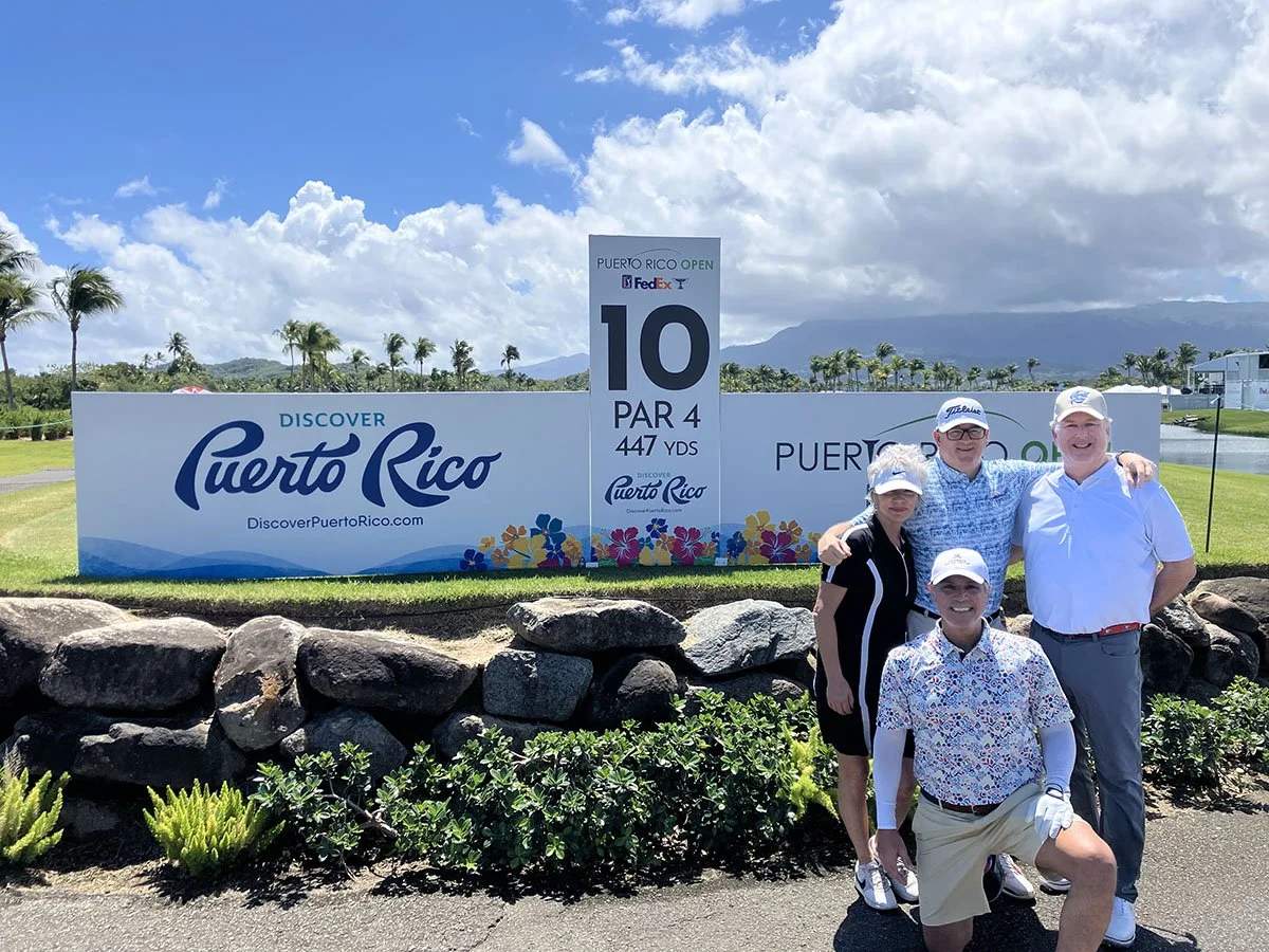 A group of four golfers stand in front of a "Discover Puerto Rico" Sign.