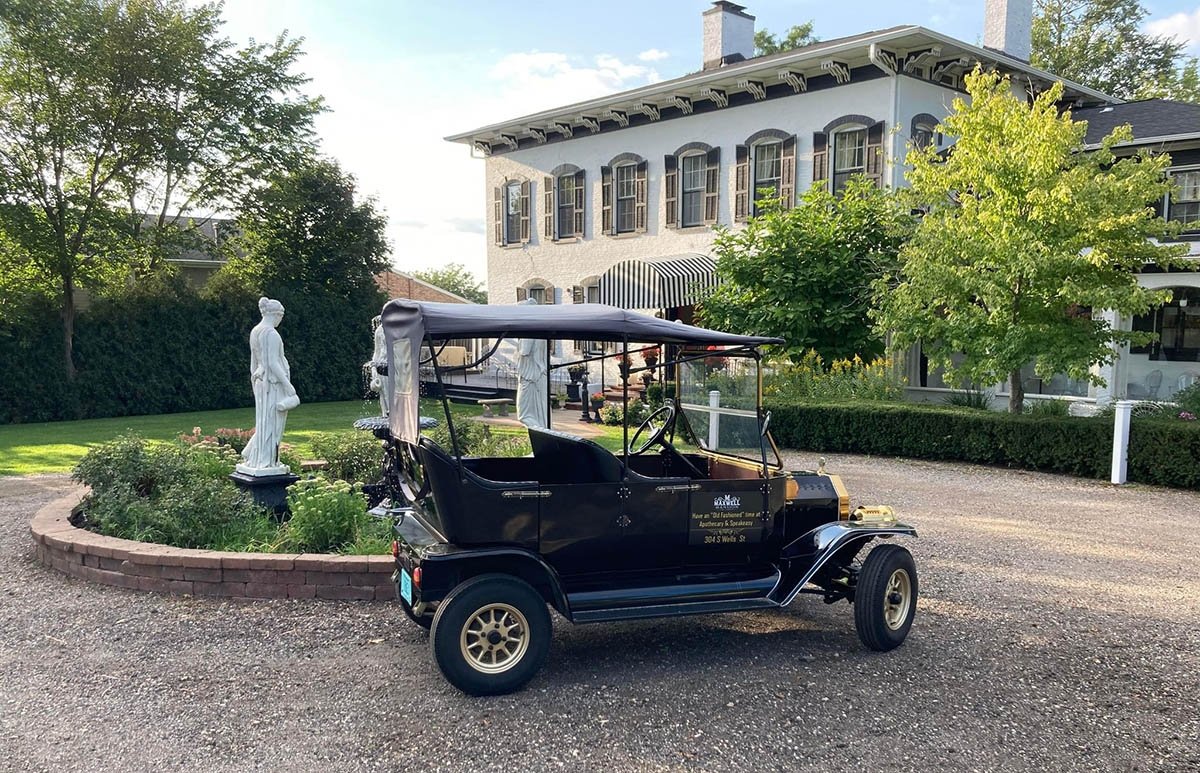 A black buggie outside a small white mansion with sculptures.