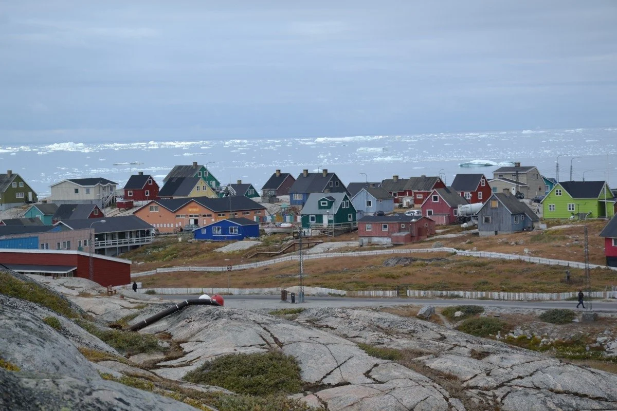 The brightly coloured houses of Illulissat sits near the ocean as icebergs drift pass.