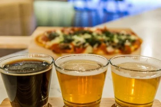 3 beers in the foreground of a pizza at the Cambria.