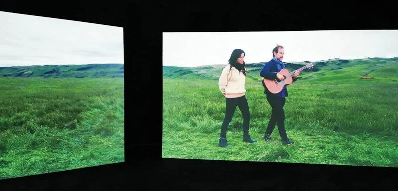 2 screens of grass with two musicians walking along.