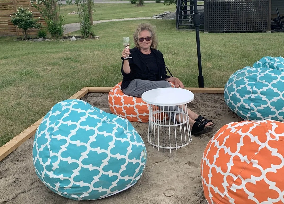 A woman holds a glass of wine while sitting on a bean bag on sand at Sanbanks Winery.