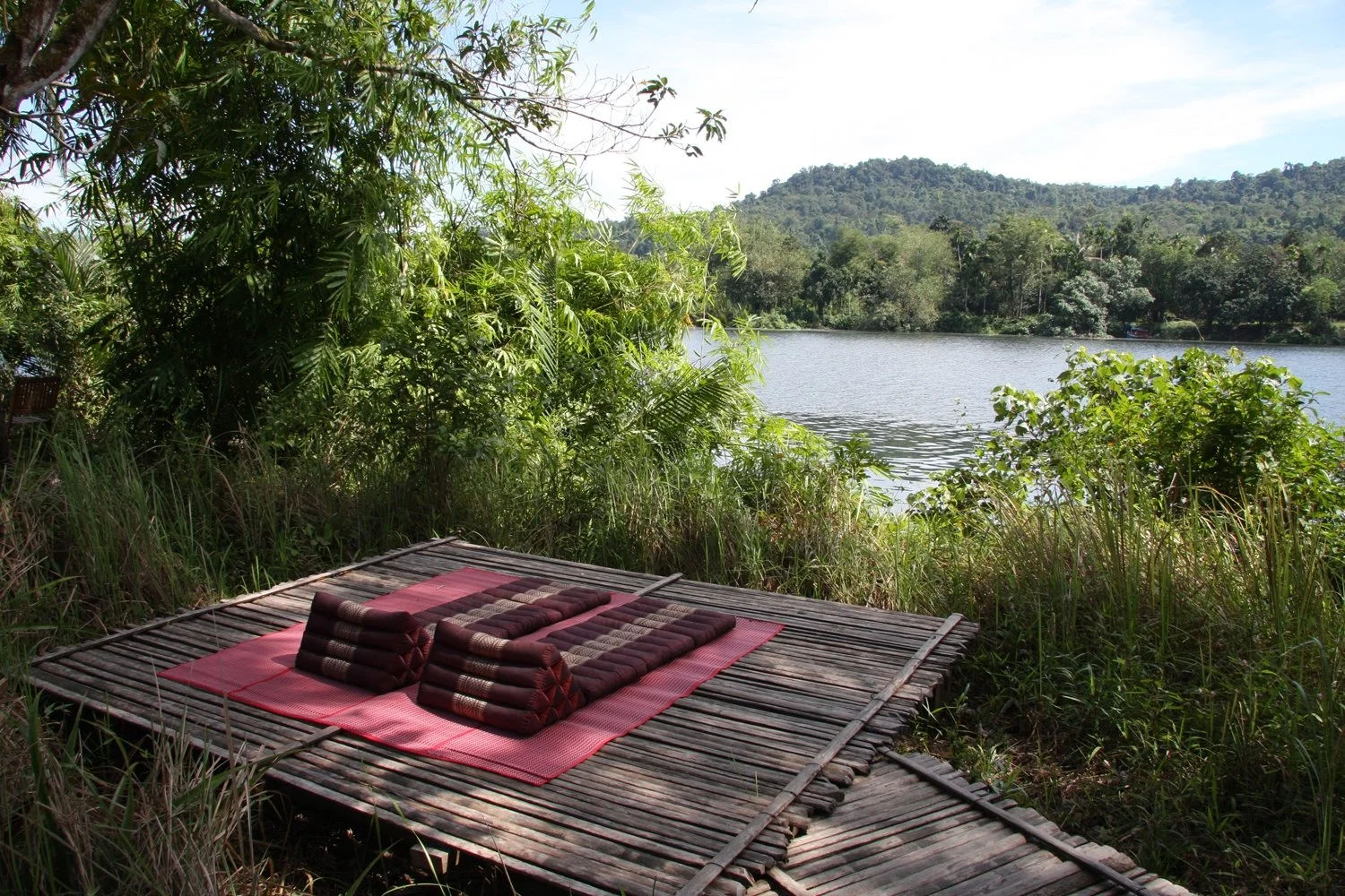Two red mats sit on a bamboo board with a fantastic view of a forest and river.