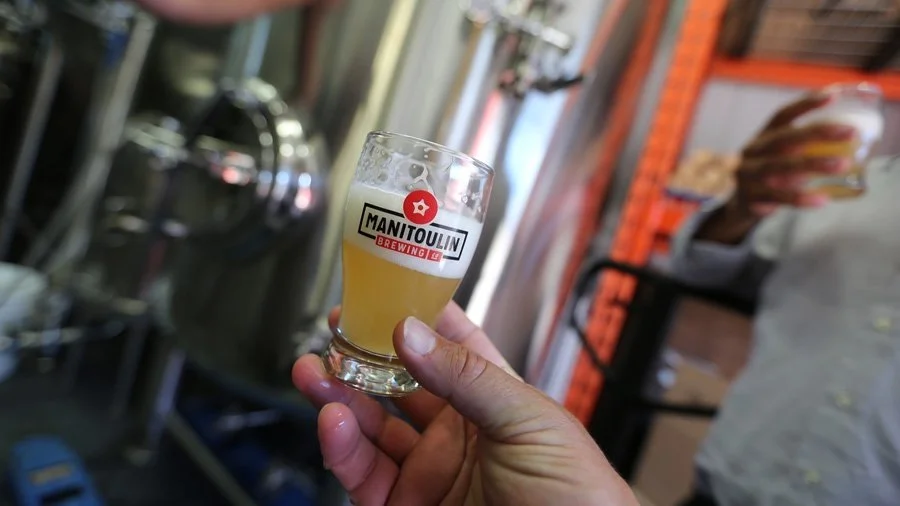 A man holds up a Manitoulin Brewing Company glass of beer.