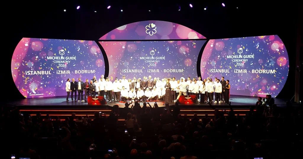 Michelin star chefs in white aprons pose in front of a purple and pink screen with the sign "Michelin Guide Ceremony"