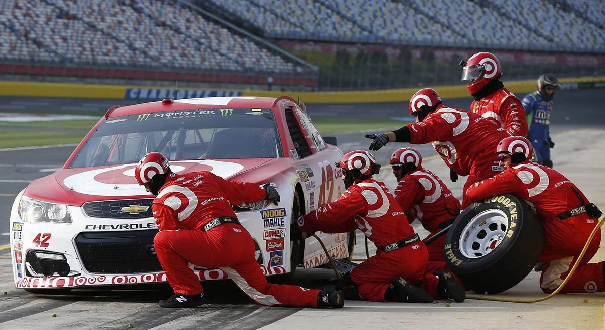 A group of mechanics change a tire on a red and white car during a NASCAR race.
