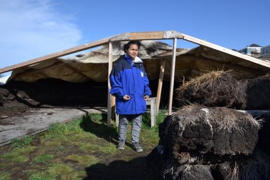 A tour guide in a long blue coat stands in front of a house.