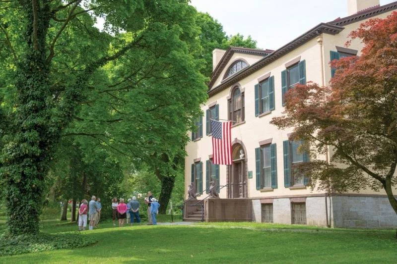 An American flag hangs outside the Seward House Museum in front of a crowd of visitors.