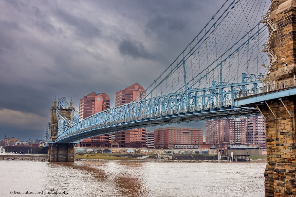 Blue railways on the John A. Roebling Bridge with brown buildings in the background.