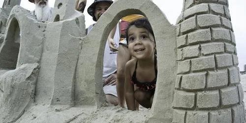 A little girl smiles through a sandcastle along the Texas beach.