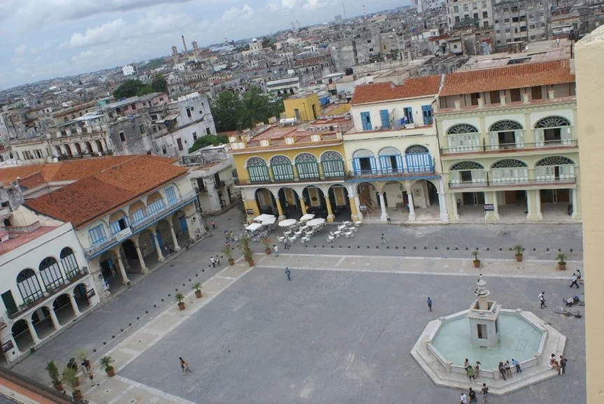 A fountain square surrounded by colored buildings and arches in Havana, Cuba.