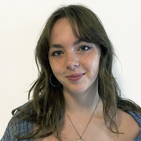 Young woman with wavy brown hair, freckles, and hoop earrings, smiling at the camera