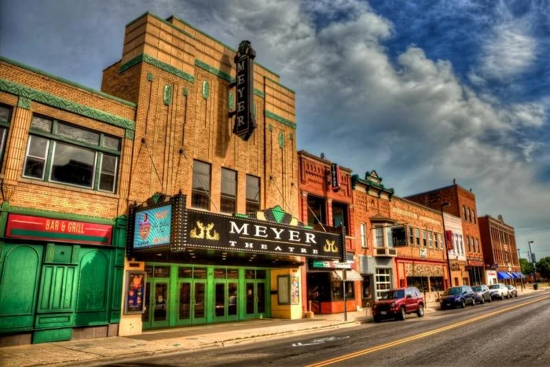 The green and wooden exterior of the Meyer Theater in Green Bay beneath a blue, cloudy sky.