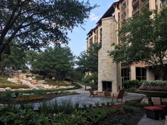 A tall brick fire place stands in front of a hotel surrounding by green trees.