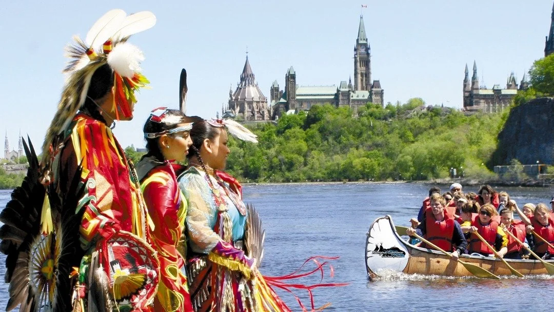 A group of indigenous people overlooking the Ottawa river with parliament in the background.