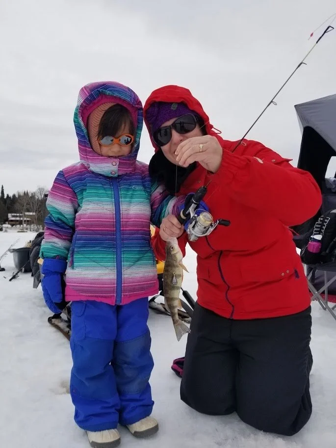 A mom and her daughter hold up a fish caught from ice fishing in Mont Tremblant.