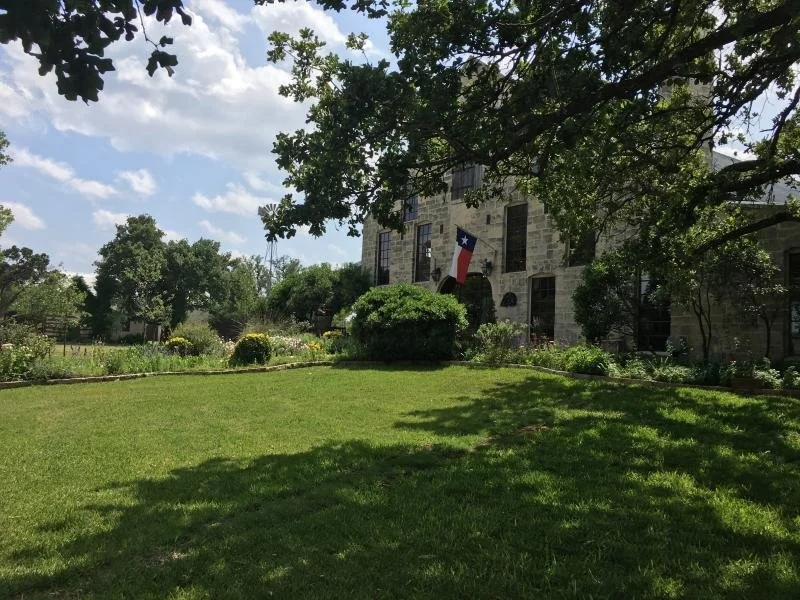 The Texas flag hangs in front of an old building surrounded by trees in San Antonio.