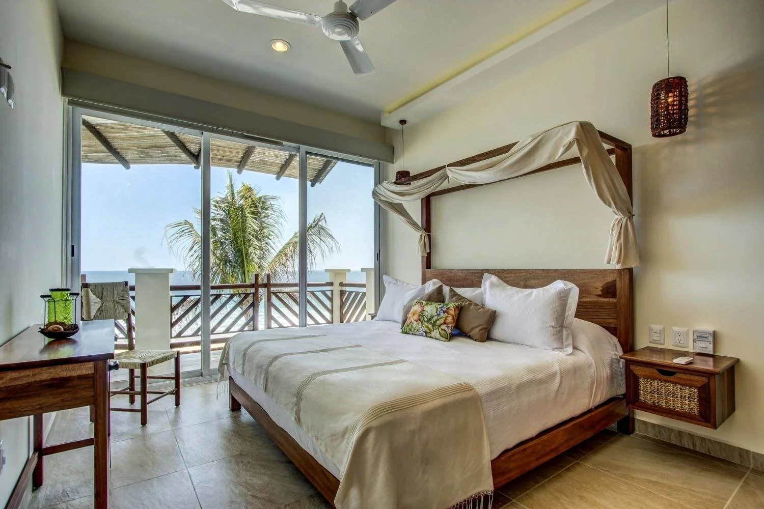 A floral pillow on a white bedspread overlooking the crystal blue sea at Vivo Resorts in Puerto Escondido.