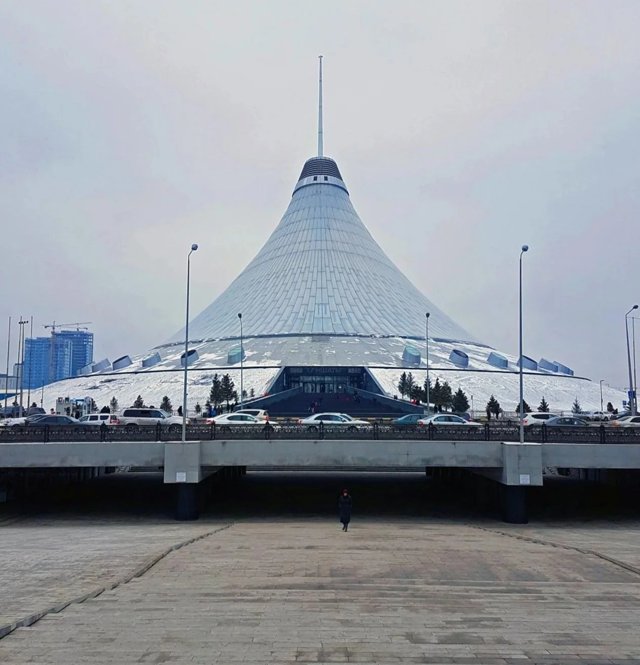 The white pointed spire of the Khan Shatyr Entertainment Center points towards the gray sky.