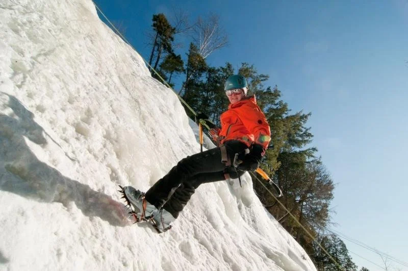 A woman in an orange jacket ice climbs in Mont Tremblant.