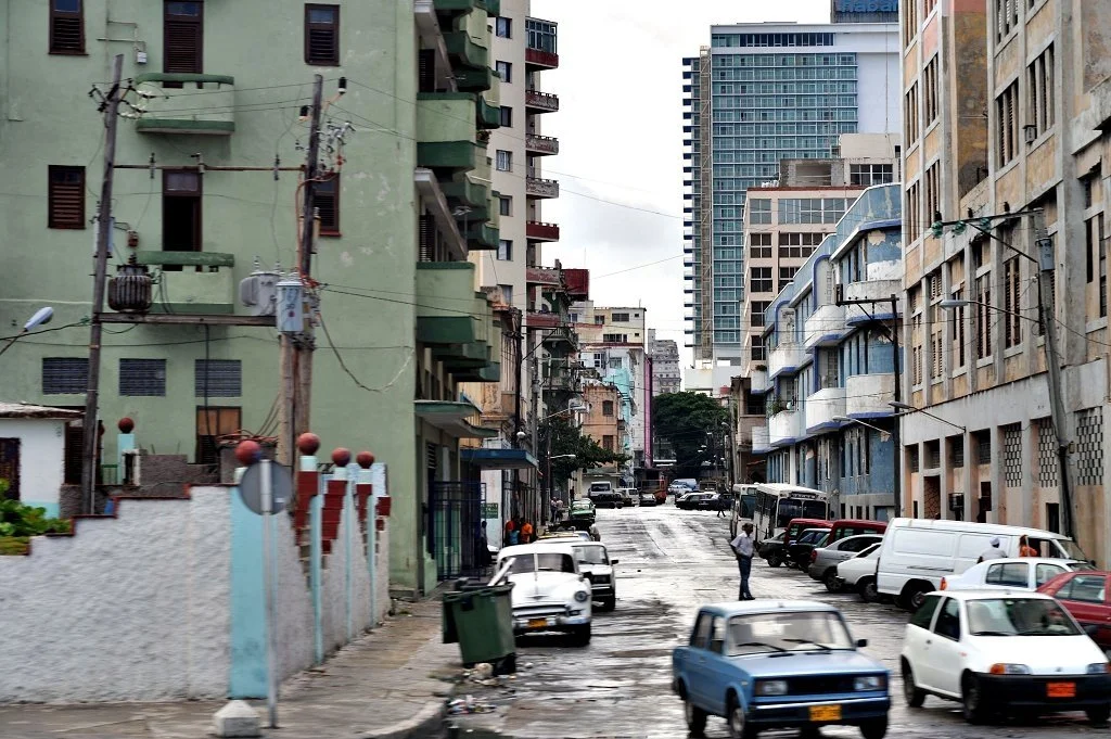 A man walks in the middle of the street surrounding by ragged buildings in Havana, Cuba.
