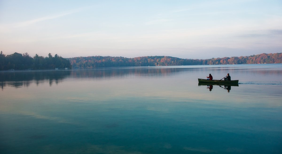 A couple kayaks through Elkhart Lake under light blue skies during fall.