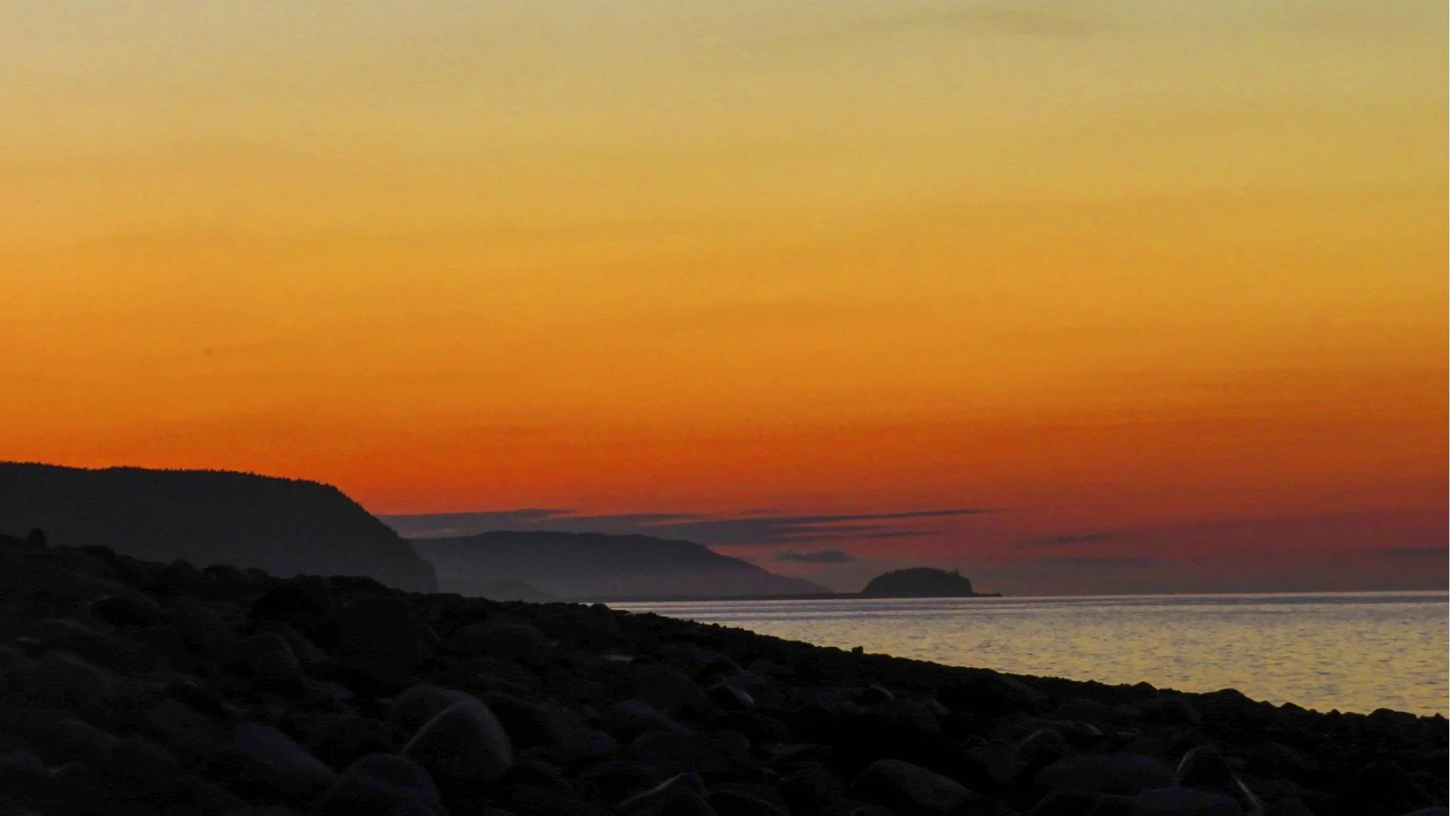 A bright orange and yellow sunset casting a black shadow over Fundy National Park.