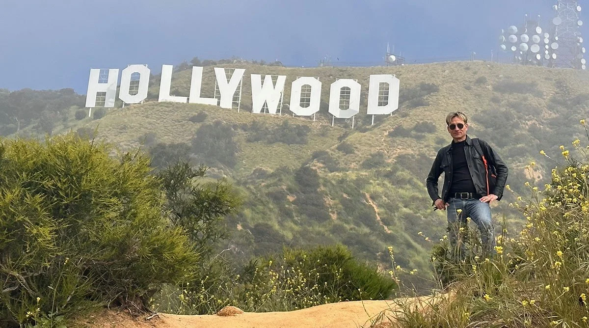 A man stands out front of the Hollywood sign.