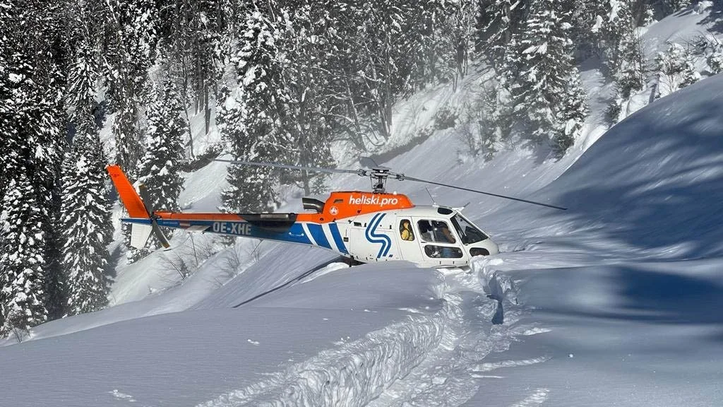 A heli ski helicopter lands on mounds of white snow.