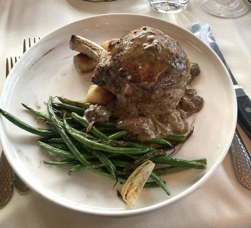 A pork chop and green beans on a white plate from Hunt Club Steakhouse.