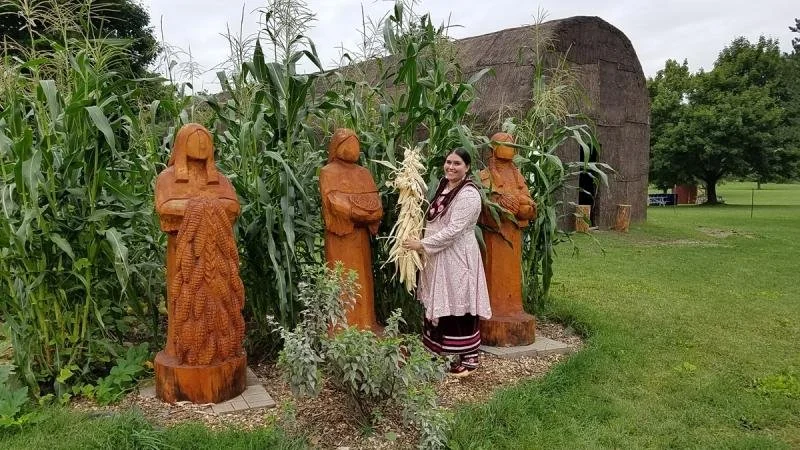An Oenida First Nation woman stands alongside a statue of the three sisters.