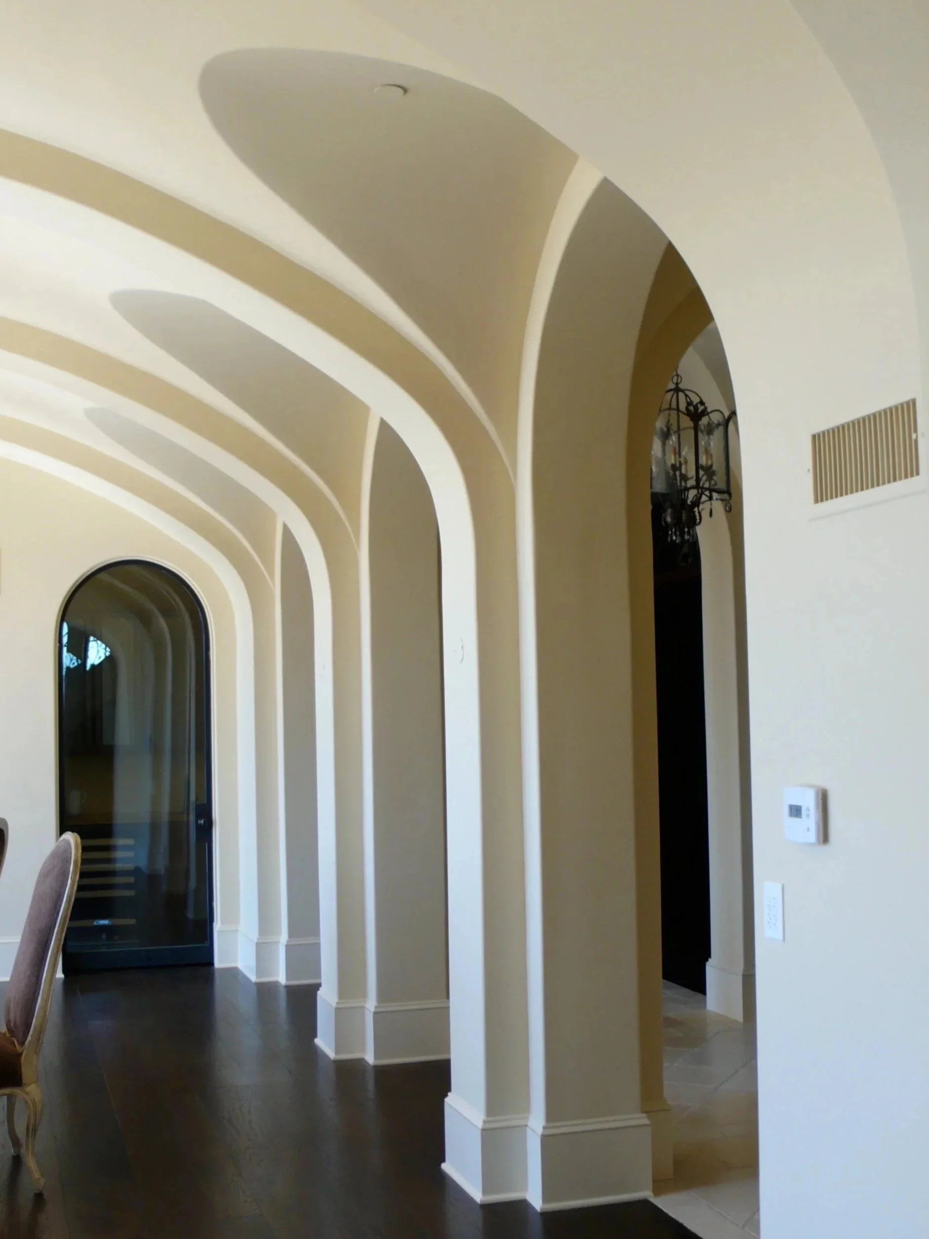 Interior hallway with venetian plaster arched ceilings, beige walls, and dark hardwood floors, leading to glass doors and a dining area.
