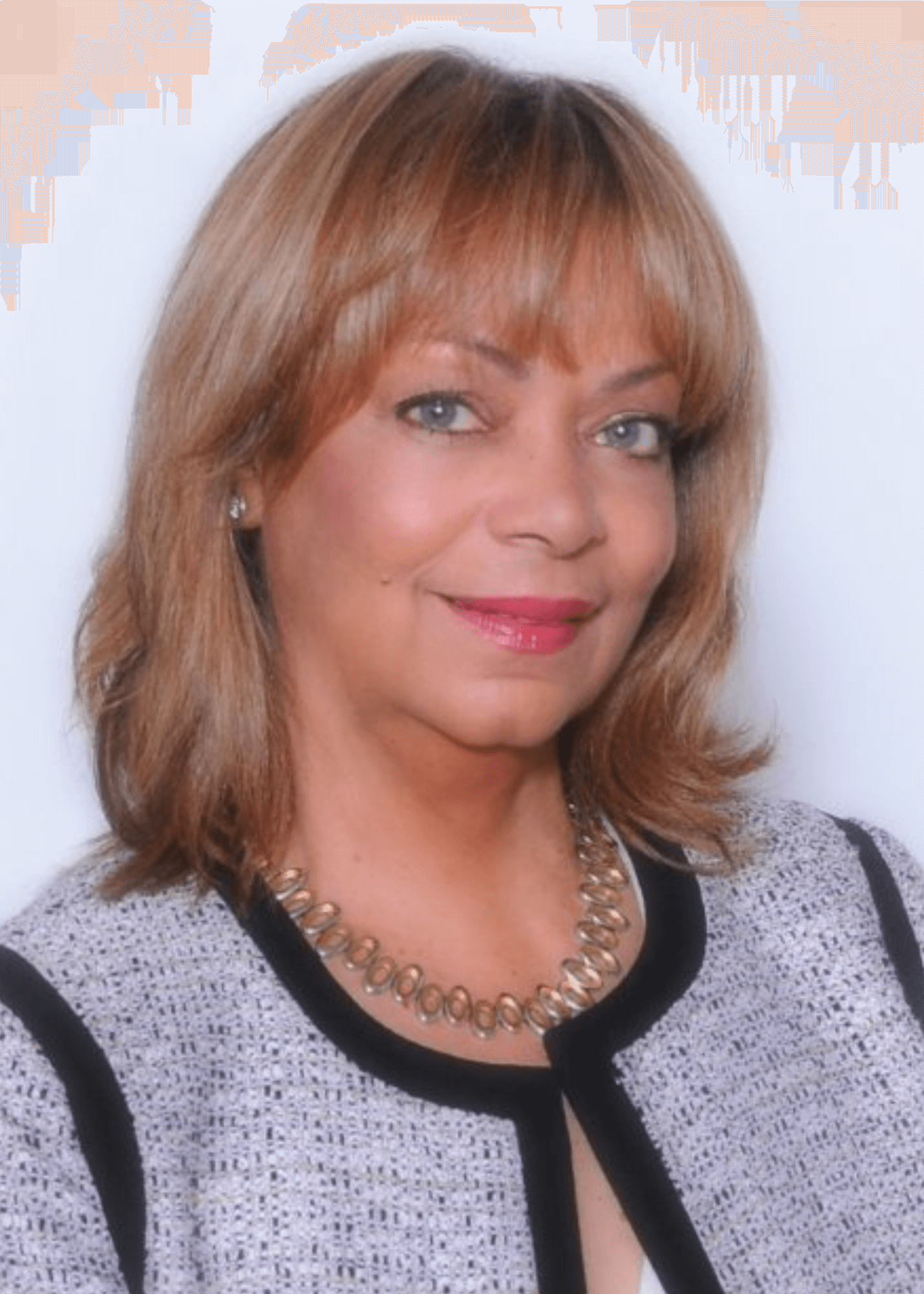 A woman with shoulder-length reddish-brown hair, wearing a textured black and white blazer with black trim, a silver necklace, and earrings, posing against a white background.