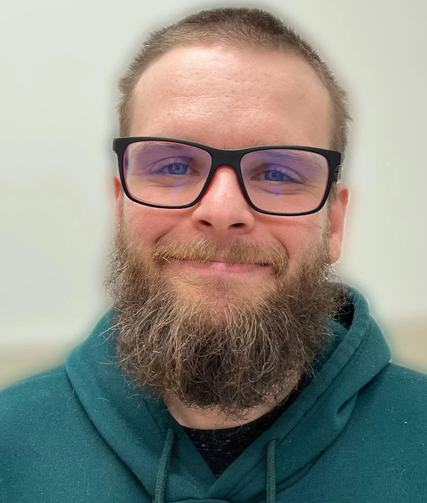 A smiling man with a beard and glasses in a teal hoodie that says 'you are enough'.