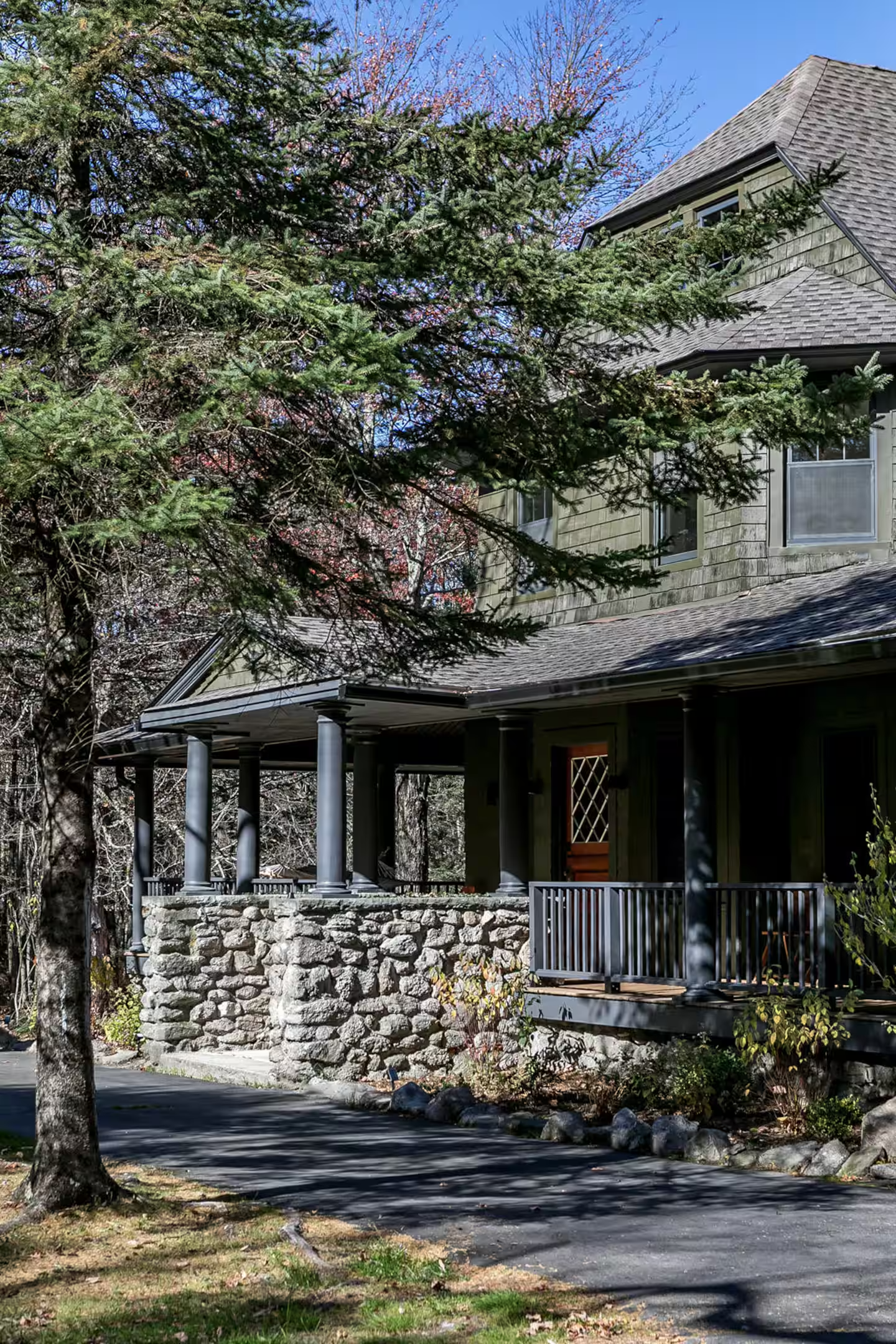 A house with a stone foundation and a porch surrounded by trees, with blue skies overhead.