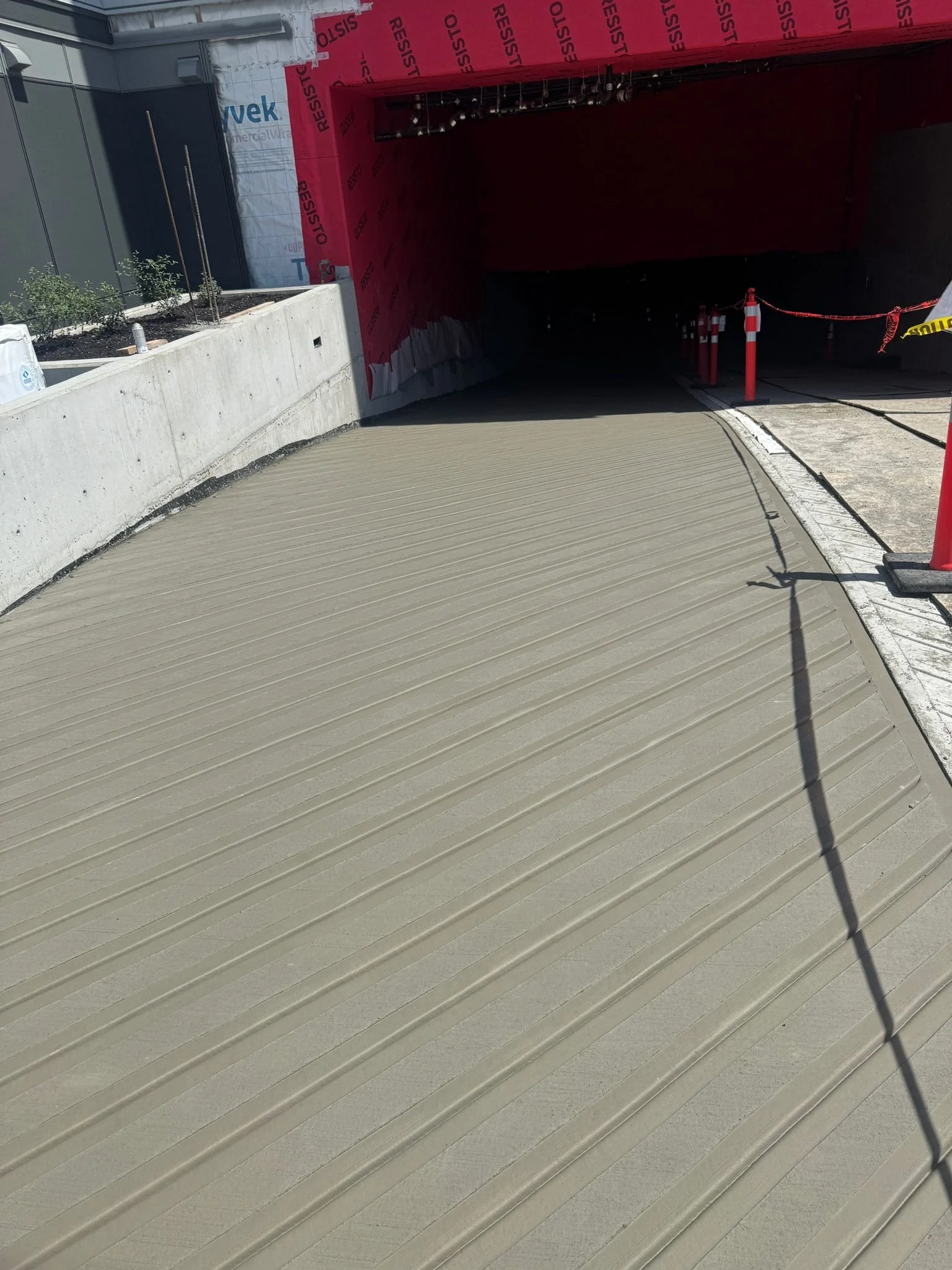 Recently poured concrete on a road entering a parking garage under construction, with construction barriers and warning signs.
