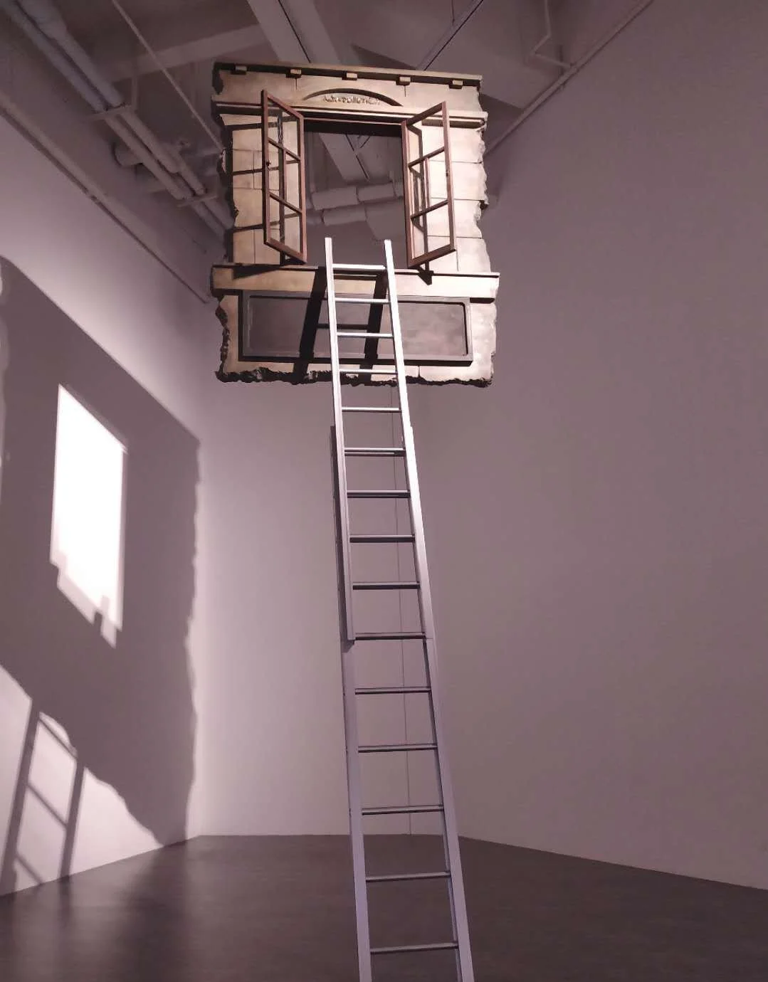 An art installation featuring a centered ladder leaning against a small, incomplete brick structure with open window frames, casting a shadow on a white wall.