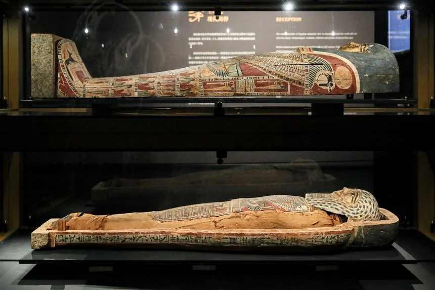 Two ancient Egyptian painted coffins displayed in glass cases, with intricate designs and hieroglyphs visible on their surfaces.